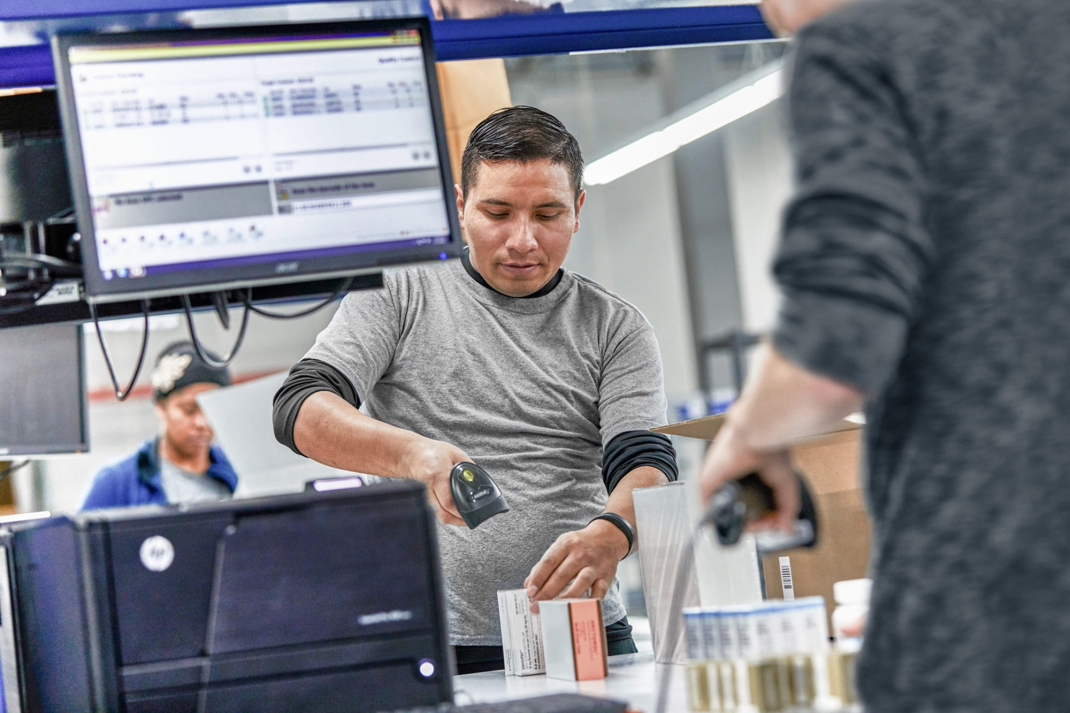 Three workers scanning small boxes of pharmaceuticals with handheld barcode readers in a warehouse.