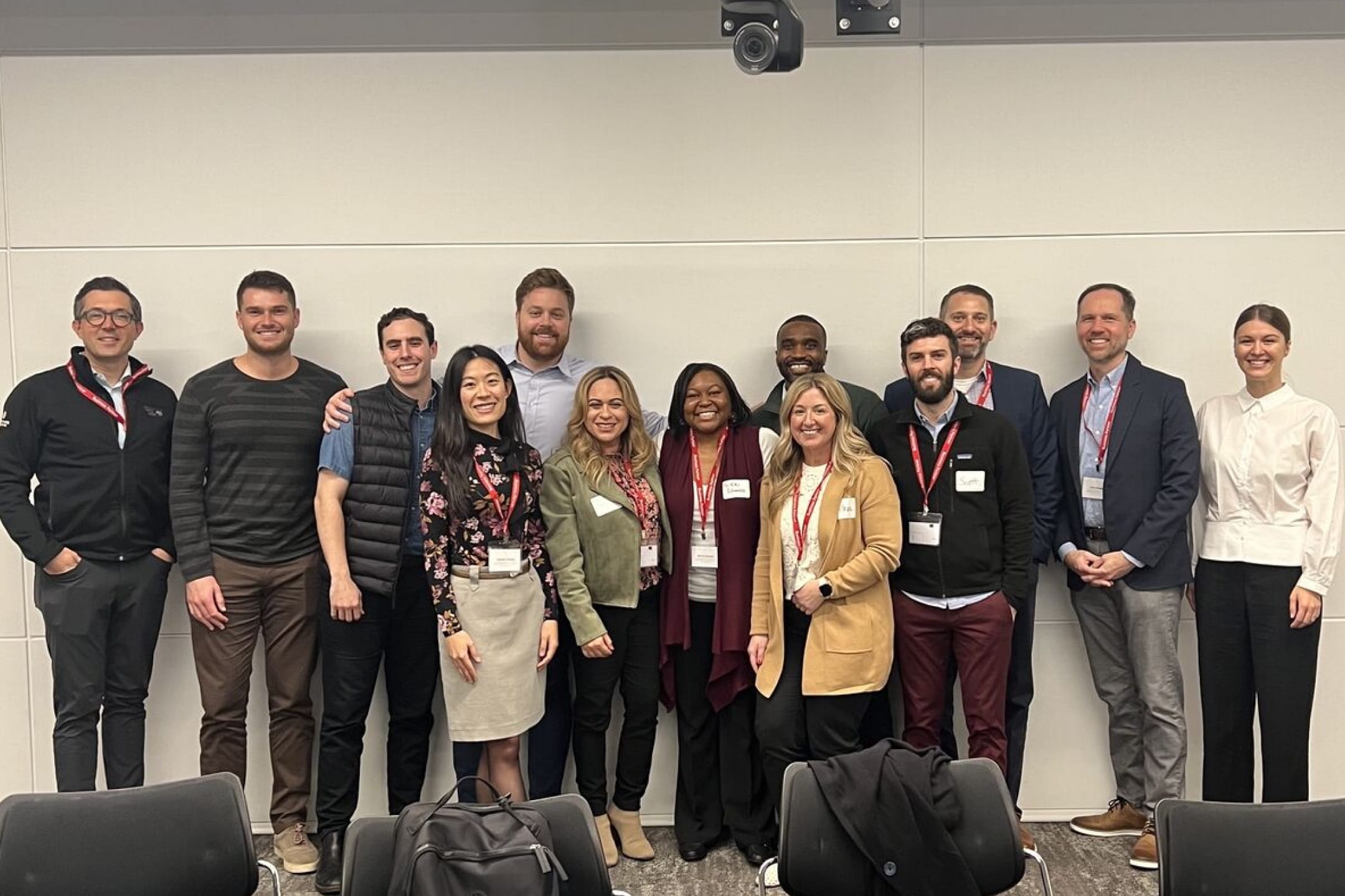 A diverse group of thirteen Cencora employees dressed casually, some with name tags and lanyards, posing for a meeting against a conference room wall.