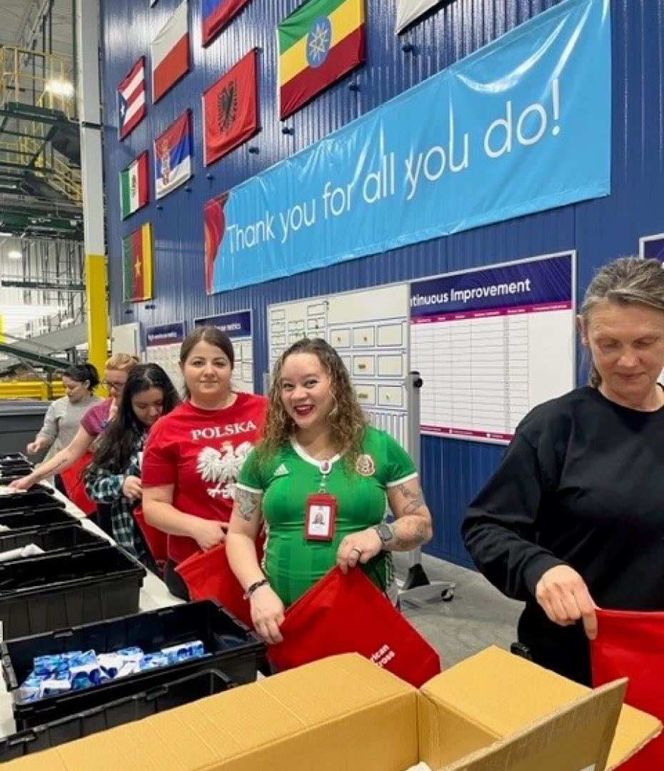 Six Cencora employees packing hygiene kits into red canvas bags inside of a warehouse. The kits were distributed to military veterans in local communities through our Red Cross partnership.