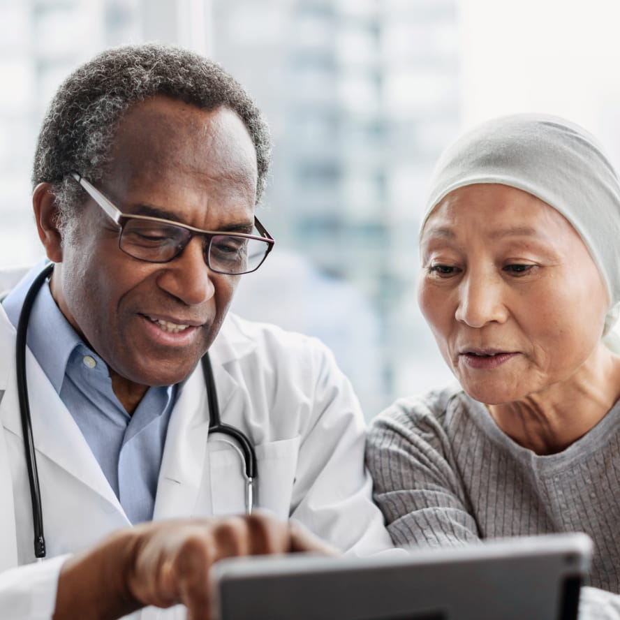 A dark-skinned doctor reviewing information on a tablet device with a patient. The patient is medium-skinned and wears a white head covering.
