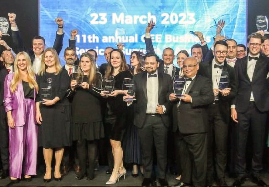 A large group of Cencora employees dressed in formal attire holding award trophies. The wall behind them reads “CEE Business Services Summit & Awards 2022. Save the date:t 23 March, 2023.