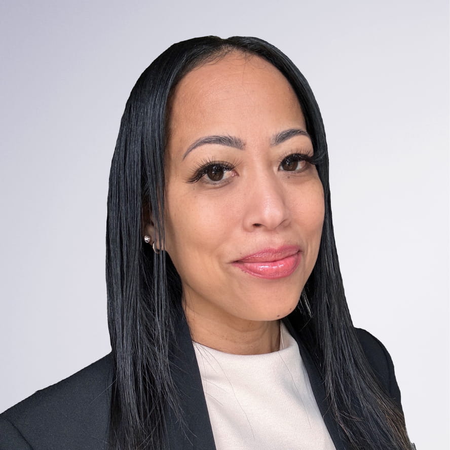 Photograph of Leia Nu. Leia, a medium-skinned person with long black hair and brown eyes, is smiling at the camera. They wear silver earrings, a white shirt, and a black jacket. They are in front of a white background.